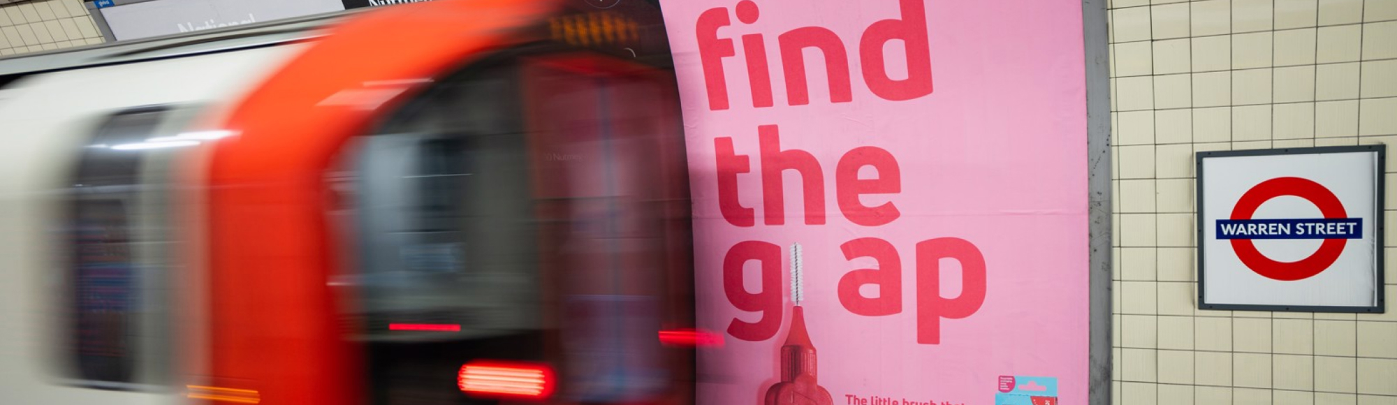 A London Underground train passes a pink TePe billboard at Warren Street station reading “Find the gap” in bold red letters.